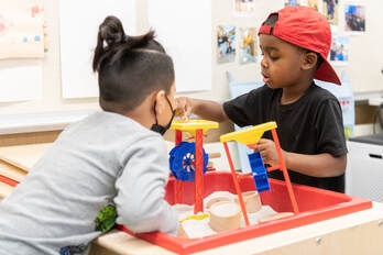 Two children play with sand and toys in an early learning classroom